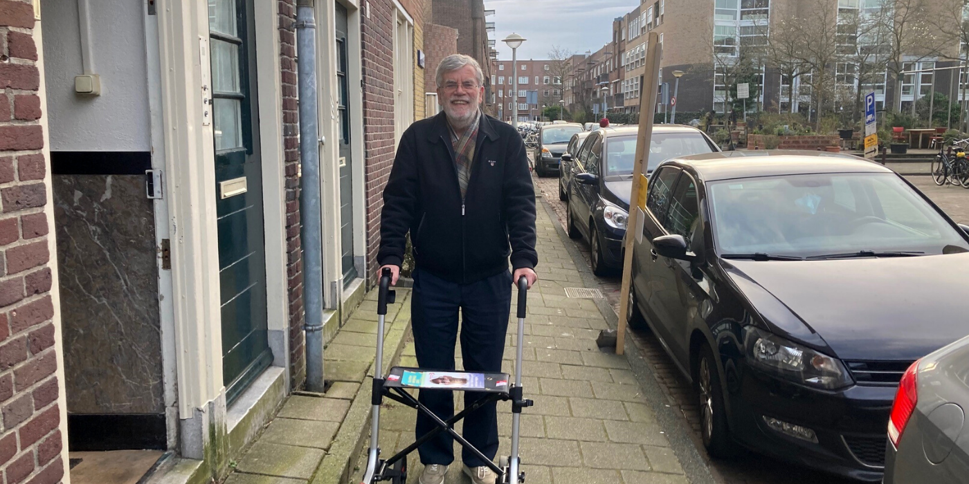Dick de Jong staat voor zijn benedenwoning in Amsterdam met een rollator