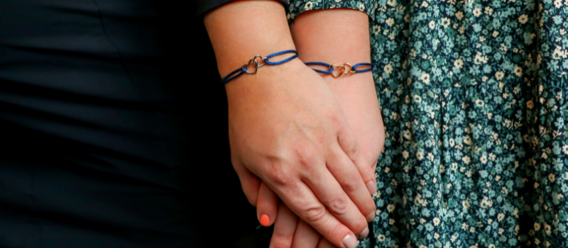 Twee vrouwen die hand in hand staan met de twee 'In Good & Bad Times' armbandjes om